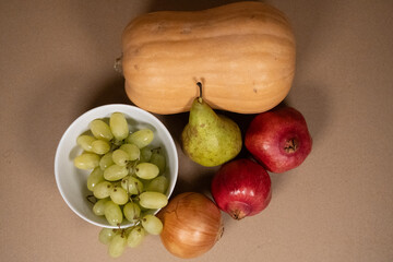 Autumn Harvest: Butternut Squash, Pear, Grapes, and Pomegranates on Brown Background