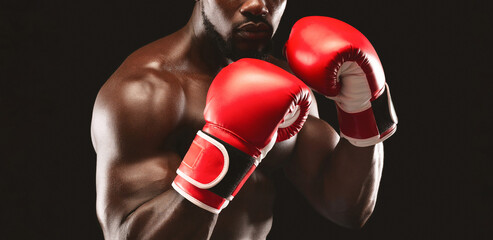 A close-up shot of a boxer wearing red boxing gloves against a black background. The boxer is...