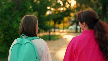 Mom walks kid with backpack to school for classes along city street. Parent mother, child daughter...