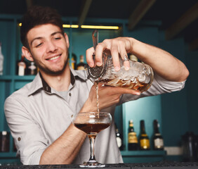 Young handsome Barman in bar interior mixing alcohol cocktail. Professional bartender at work in...