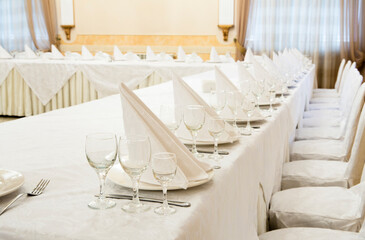 Beautifully organized event - served festive white tables ready for guests. Event in restaurant. Banquet, wedding decor, celebration. Catering and event. Wedding tables. Large restaurant hall.