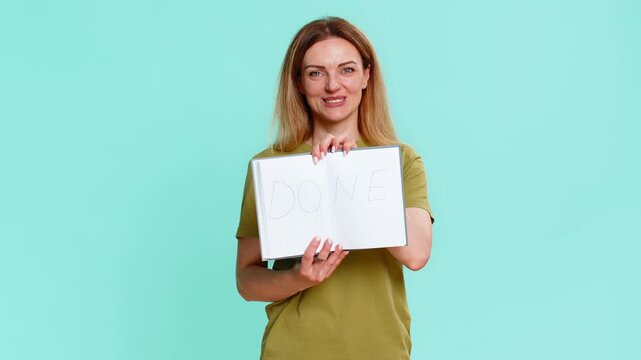 Middle-aged woman confidently shows notebook page with bold done message smiling after finishing important task or goal. Young adult girl isolated on blue background expresses pride and accomplishment