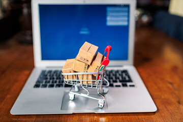 Shopping cart filled with small boxes on a laptop, symbolizing online shopping and e-commerce trends