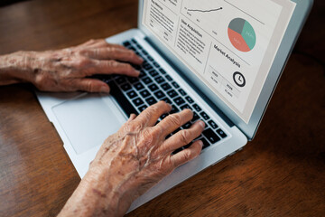 Fototapeta premium elderly person's hands typing on laptop while reviewing business reports