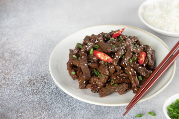 Teriyaki beef fried with sesame seeds, chili pepper, and rice on a gray background. Asian cuisine.