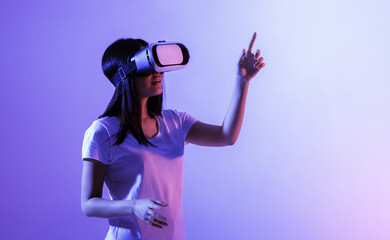 Beautiful modern girl in virtual reality glasses looks up and points a finger