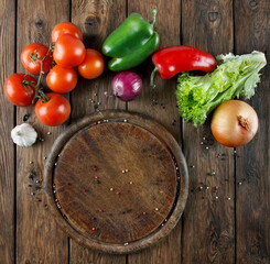 Various vegetables at wooden rustic background with copyspace on round pizza desk. Set of fresh vegetables. Vegetables top view, tomatoes, pepper, lettuce, onion, garlic, red onion. Pizza ingridients.