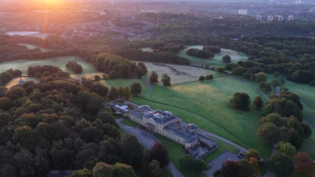 Aerial video of Heaton Park at sunrise with woodland, and Blackley suburban area of Manchester in a view.