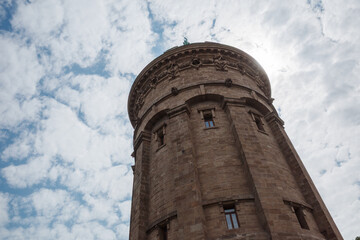 Low-angle exterior view looking up at the sandstone facade and cornice of the historic Wasserturm water tower under a blue cloudy sky in Mannheim, Germany.   © Peeradontax