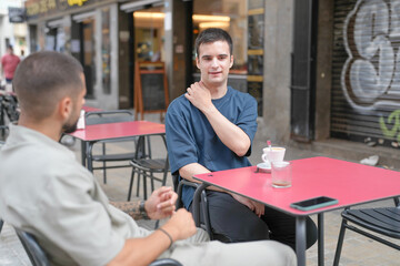 Obraz premium Two men sitting at a table in a cafe. One of them is holding his arm. The other man is looking at him