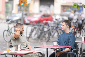 Two men sitting at a table in a cafe, one of them is wearing a shirt with a logo on it