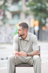 Fototapeta premium A man sits on a bench in a city street. He is wearing a shirt and pants and has a watch on his wrist. The scene is quiet and peaceful, with the man looking off into the distance