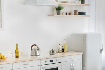 Rent flat, real estate, ready for cooking, domestic culinary, home healthy eat. White kitchen, refrigerator, stove with kettle, plate with apples, shelves with potted plants and utensils, light wall
