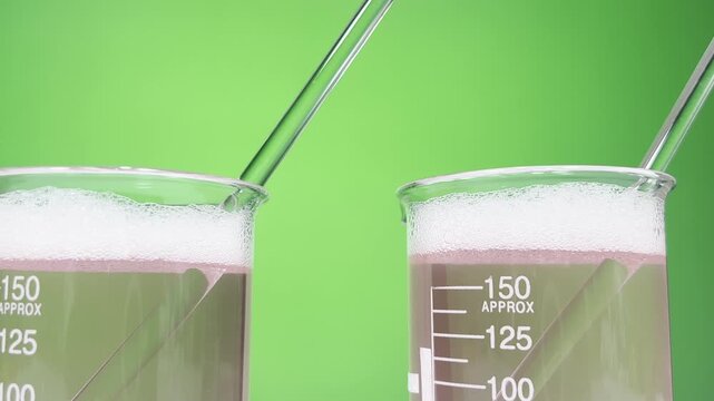 Close-Up of Foamy Pink Chemical Solution in Laboratory Beakers with Glass Stirring Rods on Green Background