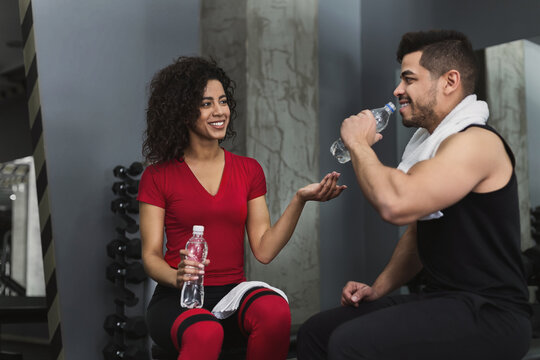 Break after training. Fitness couple having rest, talking and drinking water at gym - Powered by Adobe