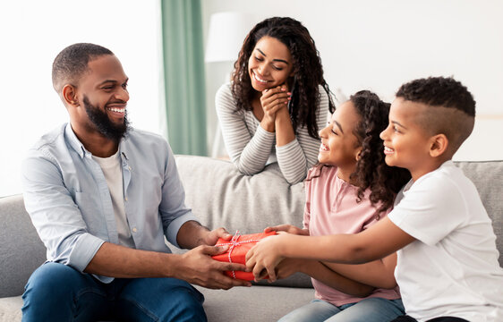 Happy Loving Family. Portrait of cheerful smiling African American dad receiving present from his little children. Girl and boy giving man wrapped gift box, greeting and celebrating Father's day