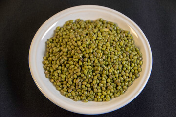 Photograph, a plate of mung bean, green gram (Vigna radiata) on black table background, it's also known as 