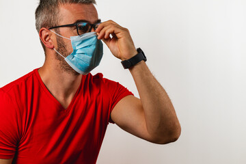 Man adjusting face mask while wearing glasses in indoor setting