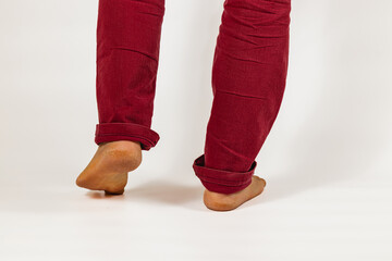 Person standing on tiptoes in rolled-up red pants against a neutral background