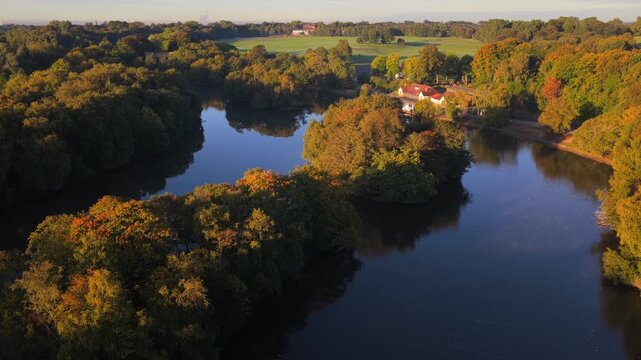 Aerial video of Heaton Park boating lake in Prestwich with tree reflections and the boat house at sunrise.