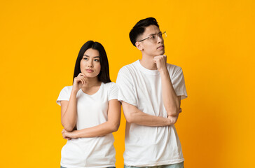 Young asian thoughtful couple posing on yellow studio background, misunderstanding in relationships