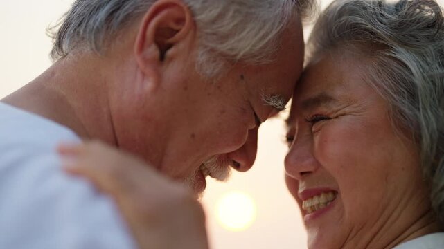 Happy Asian family senior couple dancing together on the beach at summer sunset. Healthy wellness elderly retired husband and wife enjoy outdoor lifestyle travel nature the sea with romantic moment.