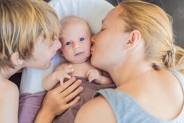 Mother and older son admiring their newborn baby in a cozy infant nest. Family bonding and sibling love concept