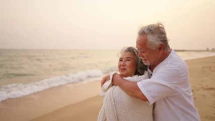 Happy Asian family senior couple relaxing by the sea at summer sunset. Elderly husband covers his wife with a blanket. Healthy retired people enjoy outdoor lifestyle travel nature ocean together. - Powered by Adobe
