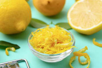 Lemon zest in bowl, fresh fruits and green leaves on turquoise table, closeup