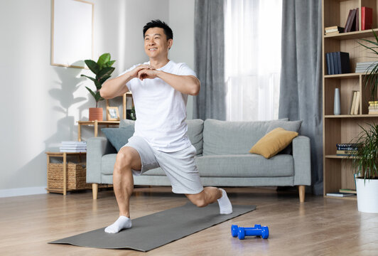 Athletic handsome middle aged asian man in white sportswear training alone at home, exercising on fitness mat, having morning yoga workout, copy space, full length shot - Powered by Adobe