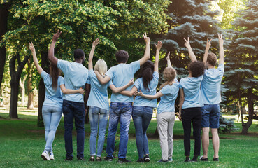 Volunteering, unity and charity. Group of volunteers embracing and gesturing in park, back view,...