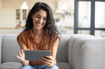 Portrait of positive young woman using digital tablet, sitting on comfy sofa at home, free space....