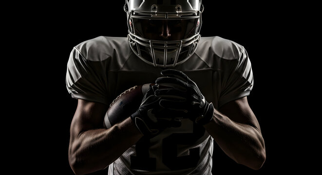 Determined football player in uniform and helmet grips the ball, ready for intense action against a dramatic dark background, embodying strength and focus.