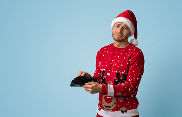 Christmas Budget Concept. Crying Young Man In Santa Hat Showing Empty Wallet, Upset Young Guy In...