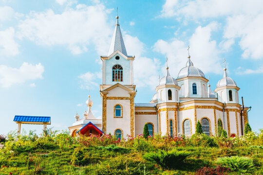  Zloti Monastery from Moldova, showcasing its ornate church and elegant domes nestled atop green hill under a bright sky. Prominent steeple and white facade stand out against the lush natural setting