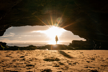 Woman standing on rock outside beach cave in vibrant morning sunshine