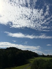 Dramatic Blue Sky with Fluffy White Clouds Over Green Hills and Forest