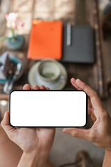 Hands holding a smartphone with a blank screen above a table with coffee and notebooks, ready for customization.