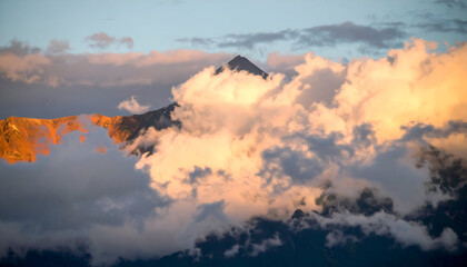 Obraz premium Majestic Mountain Peak Enveloped in Golden Hour Cloudscape Hues with Soft Warm Light and Silhouette Evergreen Trees