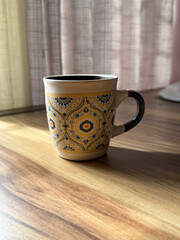 A yellow and blue coffee cup with a floral design sits on a wooden table