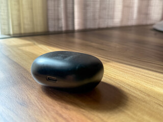 A black earbud sits on a wooden table