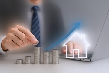 Real Estate Investment Growth Concept: Businessman Stacking Coins with House Icon on Laptop Screen, Illustrating Rising Property Value