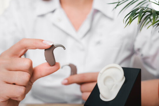 Modern digital hearing aids in audiologist hands in clinic. Doctor holding Hearing aid, near ear model for fitting and demonstration. Close-up