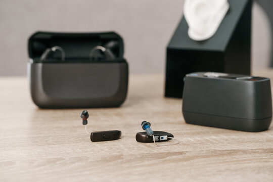 Modern digital hearing aids with charging case on wooden table in audiology clinic. Hearing aid, charger, and ear model for fitting and demonstration.