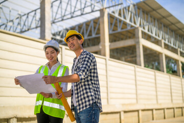 Asian engineers analyzing blueprint plan at construction site