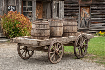 Fototapeta premium Old wooden wagon with rustic barrels in front of weathered barn, evoking vintage rural countryside lifestyle