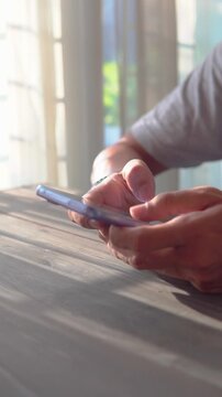 Man holding smartphone beside window while playing social media.
