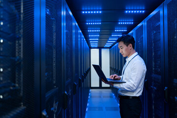 Technician working on laptop in a data center server room illuminated by blue lights