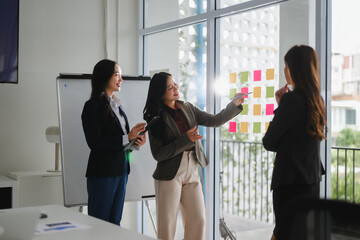 Businesswomen brainstorming ideas using sticky notes on glass wall