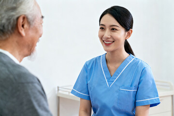 A female healthcare professional in blue scrubs smiling while interacting with an elderly patient in a clinical setting.